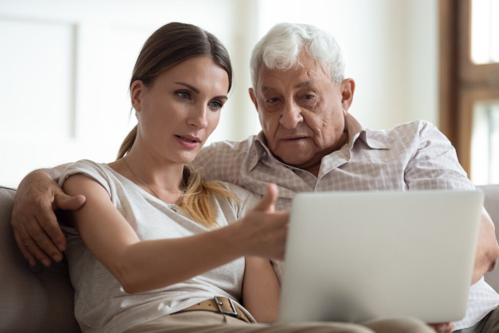Adult daughter reviewing senior care options online with her elderly father while sitting together at home.