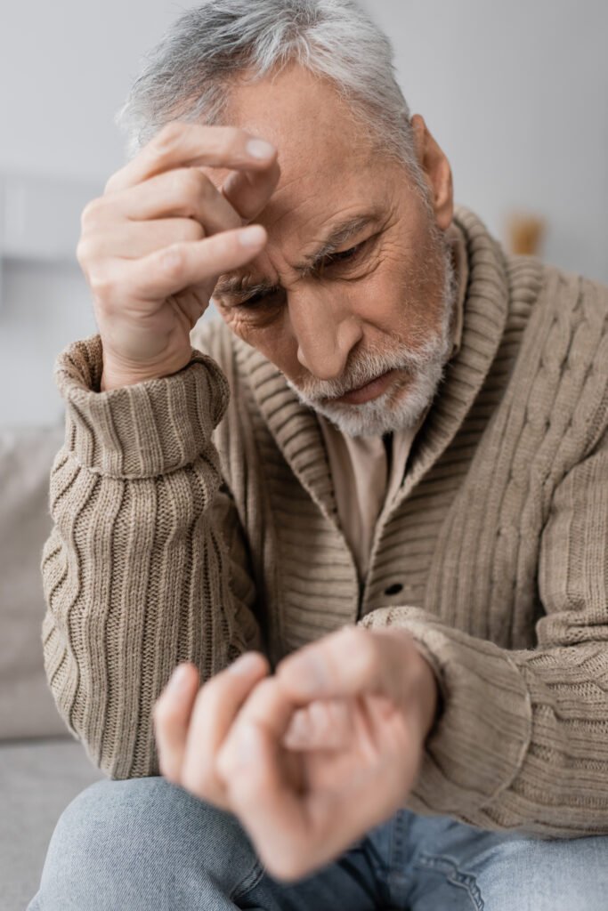 Senior man looking closely at his hand with concern, representing early Parkinson’s disease tremor symptoms.