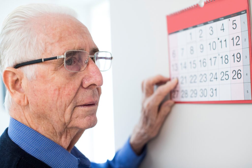 Older man with memory loss looking at a calendar while experiencing possible early signs of Alzheimer’s disease and confusion about dates