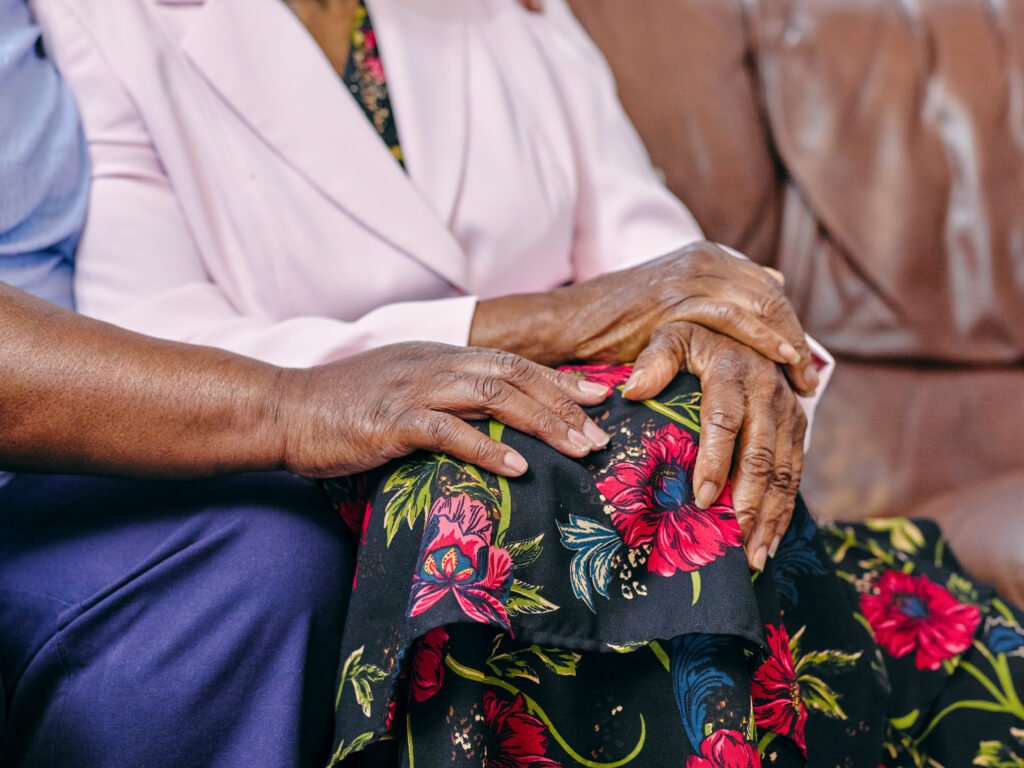 Adult daughter gently holding her elderly mother's hand while providing care at home through family caregiving support in Michigan.
