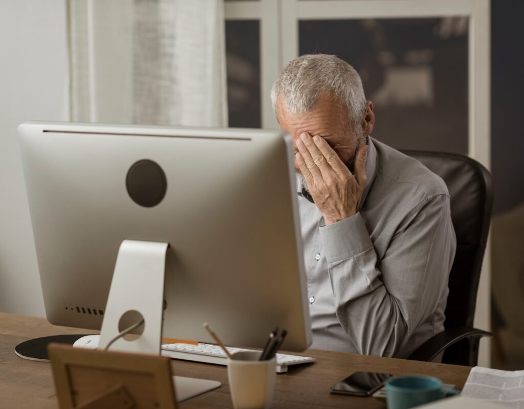 Caregiving while working: Exhausted family caregiver feeling overwhelmed while working at a computer.