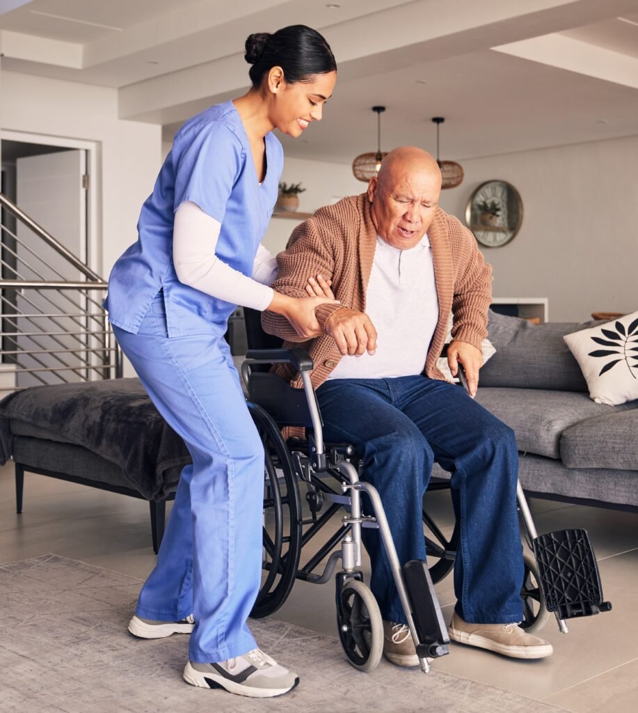 Caregiver helping an older adult with dementia stand from a wheelchair as walking and mobility become more difficult.