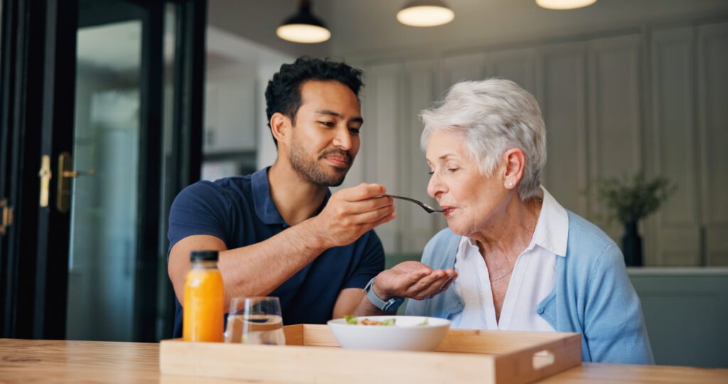 Family caregiver gently offering food to an older adult with advanced dementia during a comfort-focused meal.