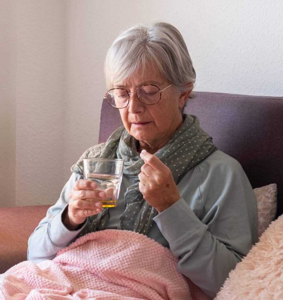 Older woman with dementia taking medication and drinking water as swallowing difficulties become more common in advanced dementia.