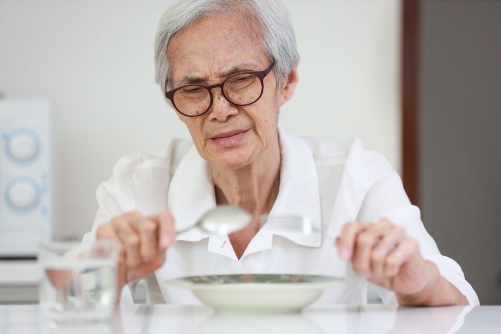 Older adult with dementia struggling to eat a meal, illustrating why people with dementia stop eating as the disease progresses.